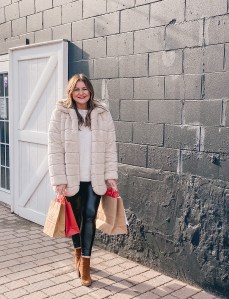 girl standing outside in a faux fur coat with Christmas shopping bags