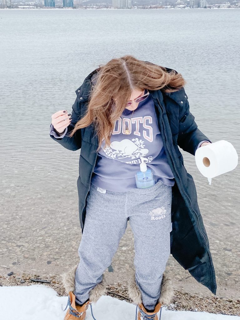 Woman on the beach in a track suit holding toilet paper and hand sanitizer